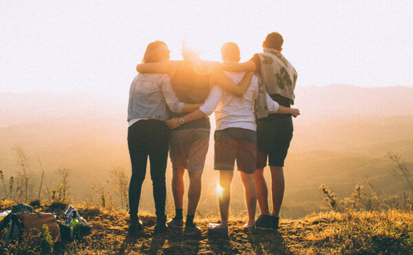 Group of friends embracing at sunset on a hilltop, sharing joy and connection.